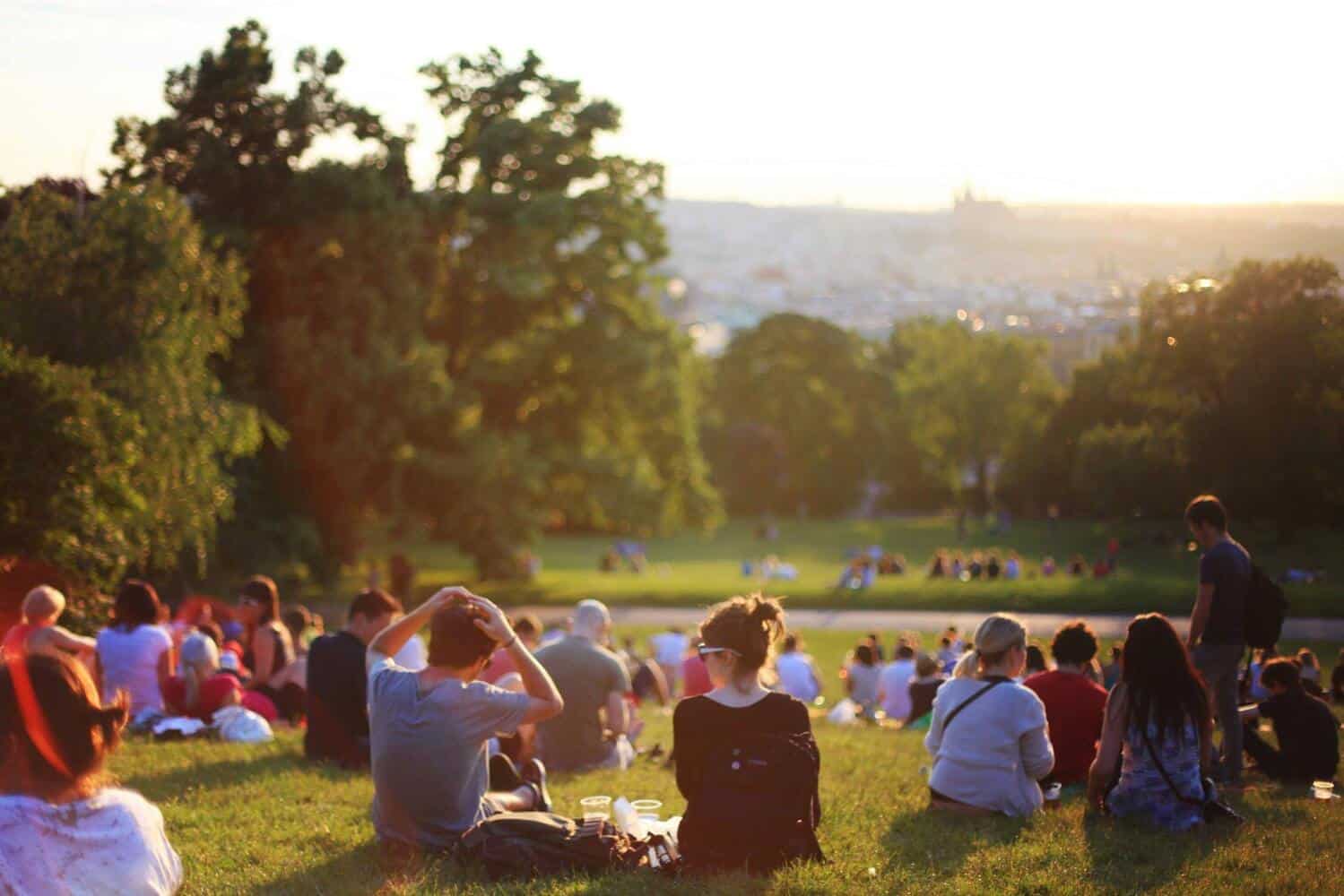 People sitting on a grassy hill during sunset, enjoying the view.
